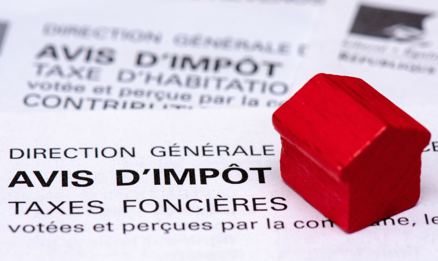 Avis de taxe foncière avec une maison miniature rouge posée dessus.