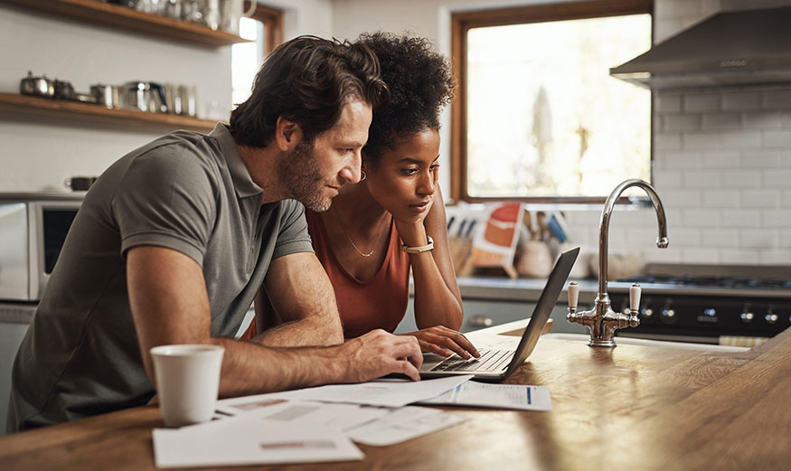 Une femme et un homme regardent avec attention un écran d’ordinateur, avec des papiers administratifs à côté