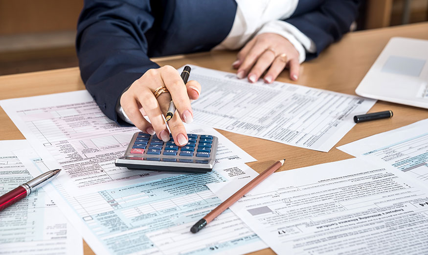 Mains de femme pianotant sur sa calculatrice, avec documents d’impôts sur la table