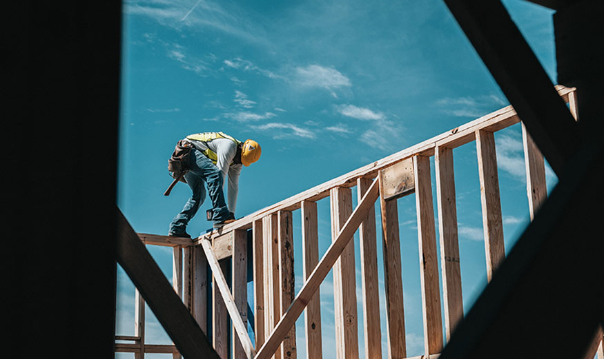Homme avec un casque de chantier sur une structure de maison en bois.