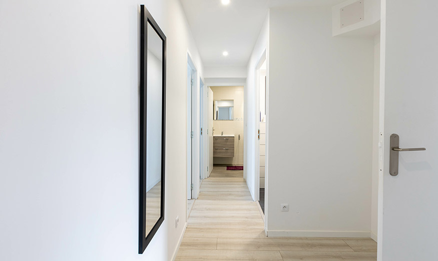 Long couloir d'un appartement neuf au mur blanc, avec miroir et plusieurs portes.