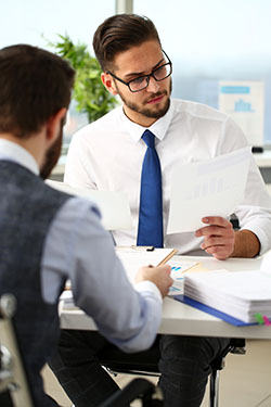 Deux hommes en costume assis à un bureau face à face consultent des rapports