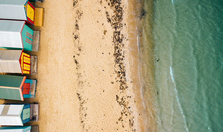 Vue aérienne en plongée sur une plage avec maisons de plage face à la mer.