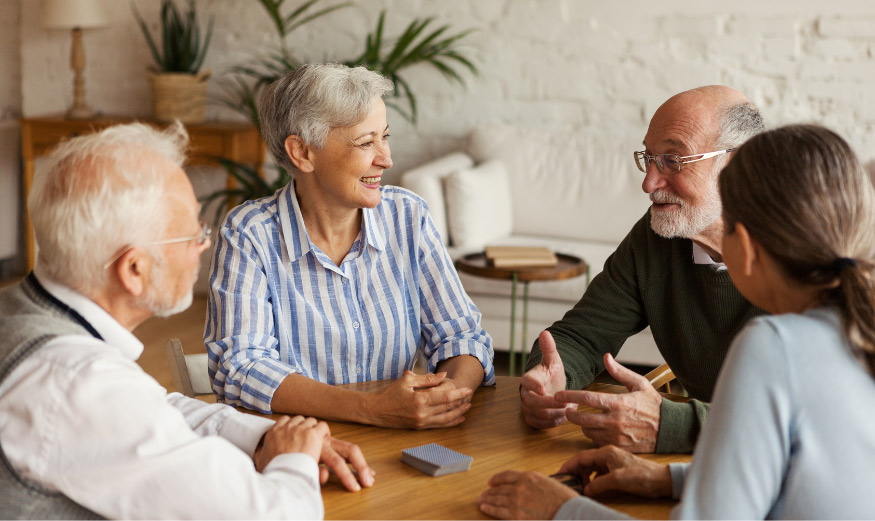 Groupe de quatre amis seniors joyeux, assis à une table dans une résidence de services pour seniors.