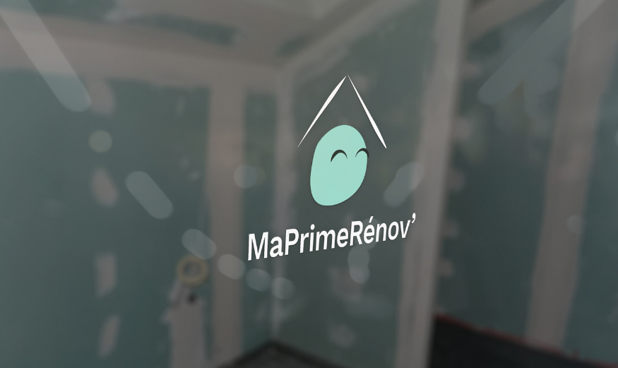 Focus sur le logo MaPrimeRenov sur une fenêtre, dans un arrière-plan flou d’une maison en construction.