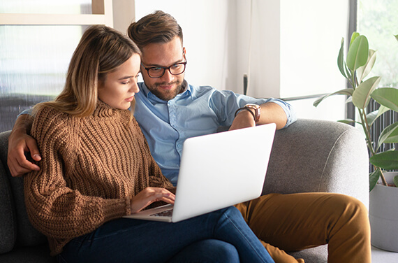 Un couple assis sur un canapé consultent leur ordinateur portable