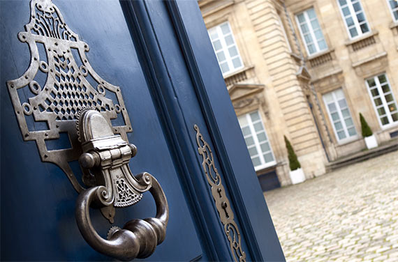 Une porte ancienne bleue avec un bel heurtoir ouverte sur une cour pavée donnant sur un bâtiment ancien