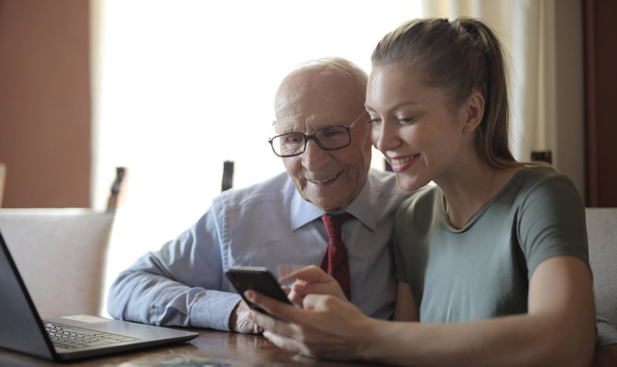Homme âgé et jeune fille souriants regardant un téléphone.