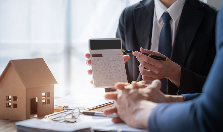 Un personne montrant à une autre une calculatrice avec une maison miniature posée à côté.